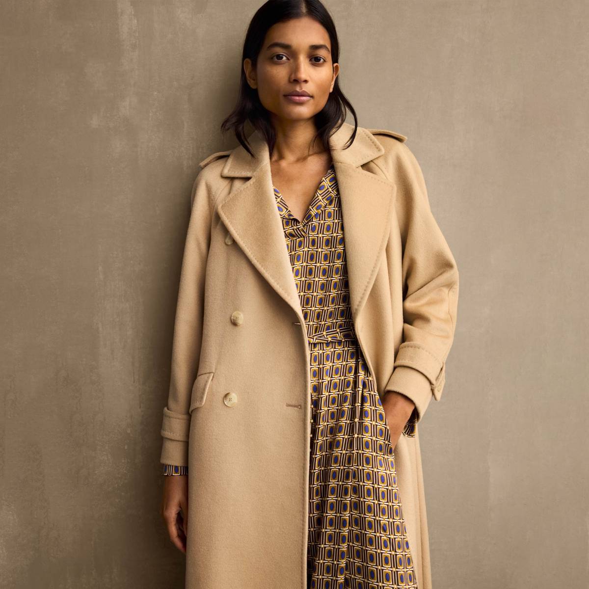 Woman wearing camel-coloured coat and patterned dress. Shop women’s Jaeger